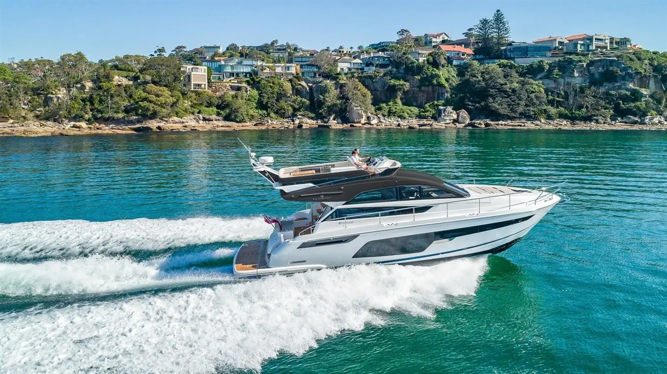 A luxury motor yacht cruising through clear turquoise waters, with scenic coastal homes in the background.